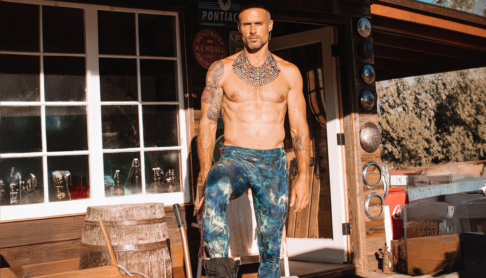 An image of a man without a shirt wearing a pair of blue and green foil leggings.  