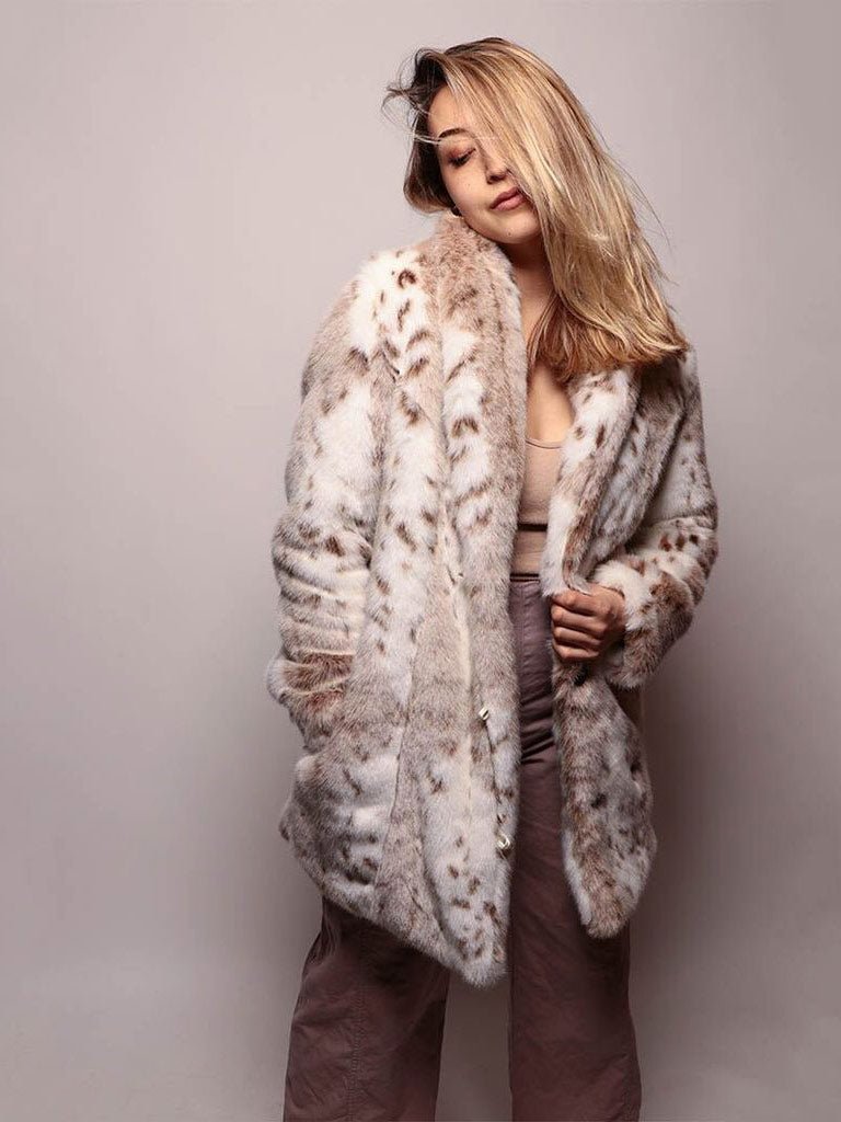 A blonde girl, with her eyes closed and hair swept to one side, has a cozy expression on her face as she poses with her hand in the pocket of a vegan Siberian snow leopard fur coat.