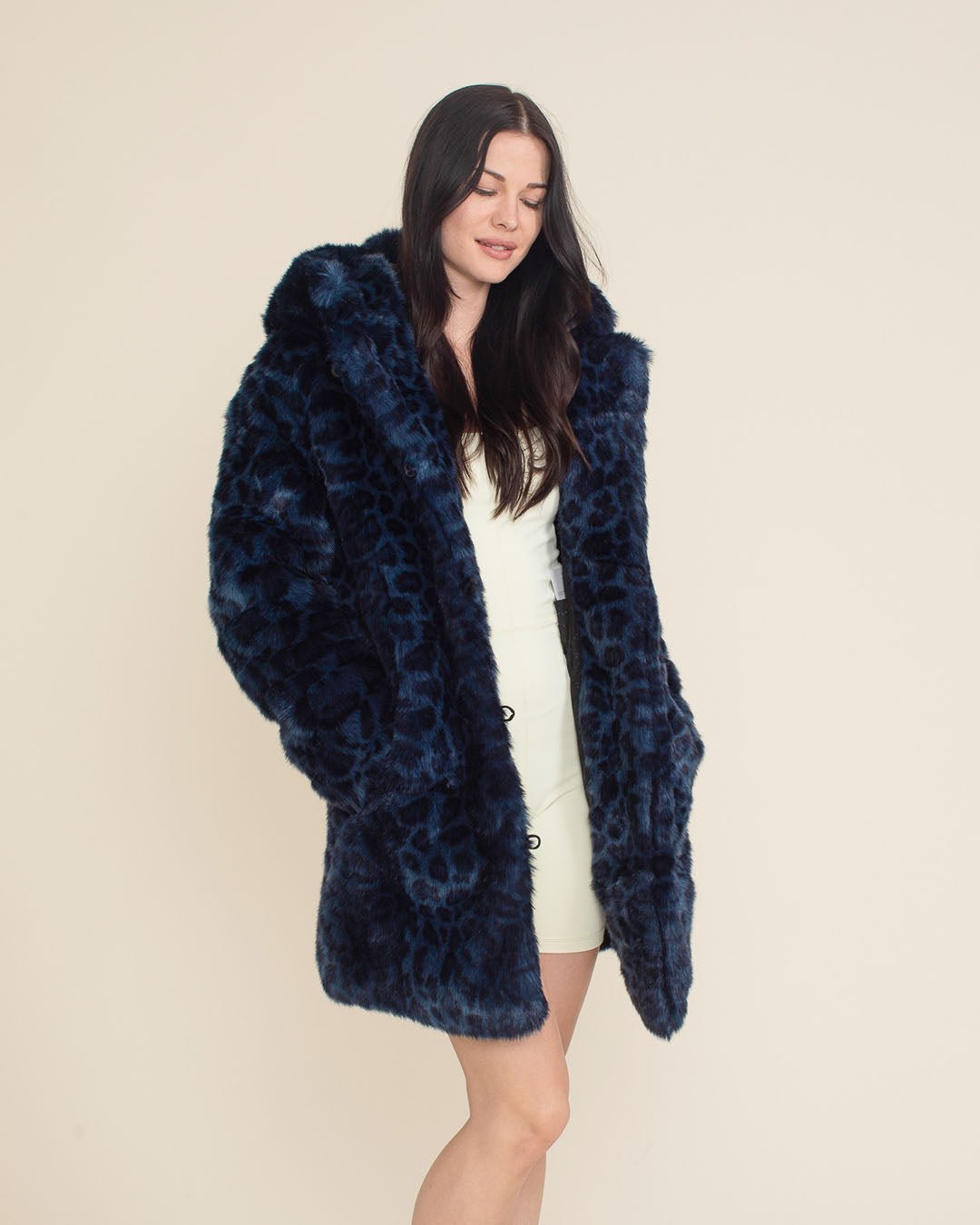 Dark-haired pretty model with eyes closed in thought, wearing the Indigo Leopard Collector Edition Classic Faux Fur Coat, hands in pockets. Elegant and serene.