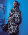 Guy leans against blue wall, knee bent, holding lapels of Himalayan Snow Leopard Faux Fur Jacket. Stylish and edgy.