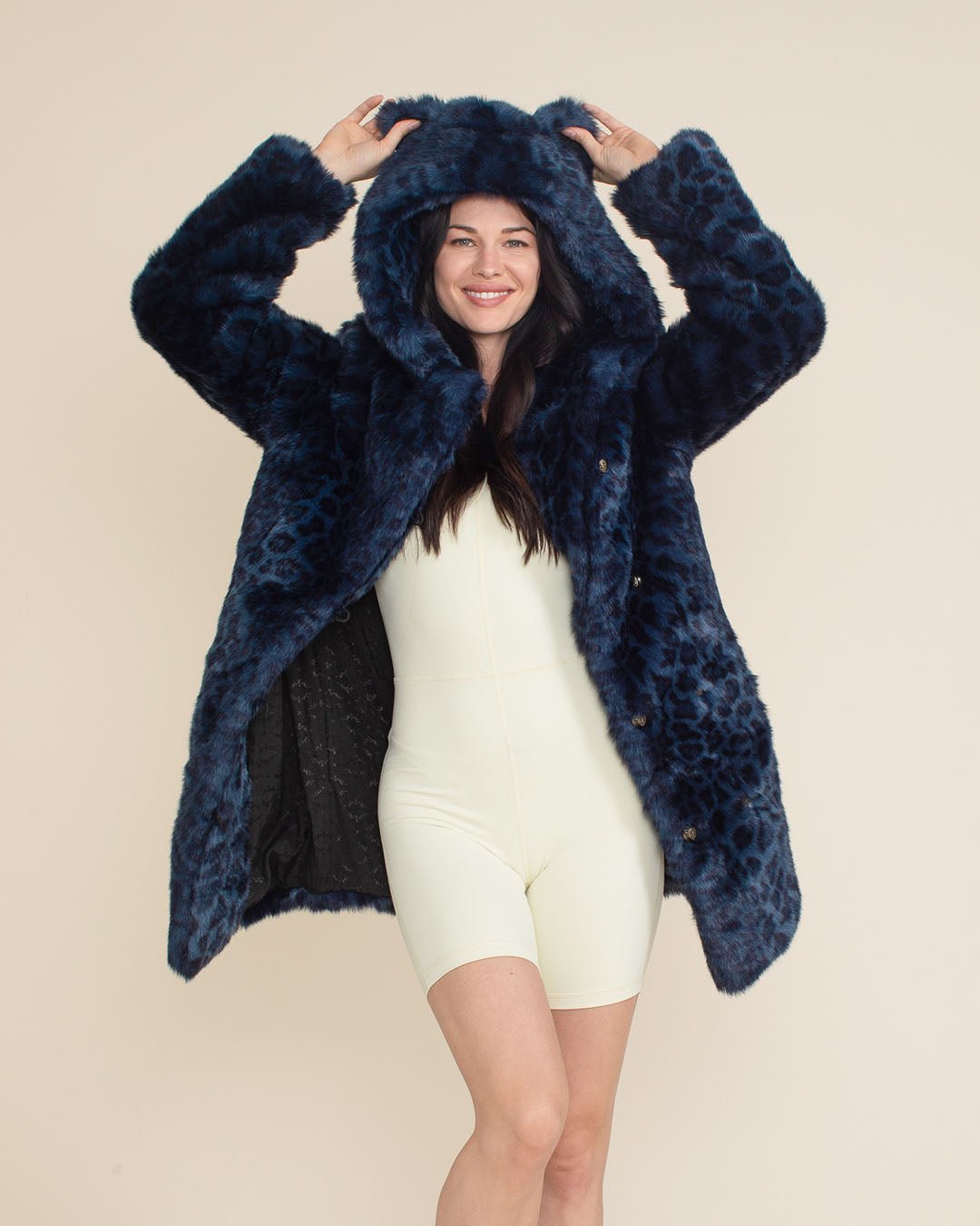 Playful, smiling dark-haired beauty holding the ears of the hood on the Classic Indigo Leopard Collector Edition Vegan Fur Coat. Fun and stylish.