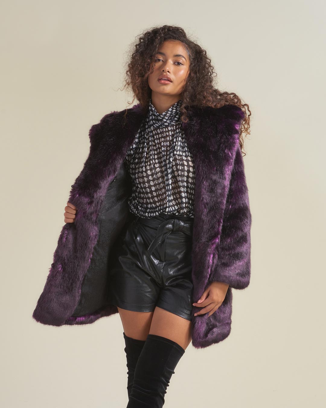 Curly haired female model wearing midnight wolf fake fur jacket and holding the right side of the coat open to show black liner. 