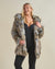 A curvy, flirty, smiling blonde girl rocking a realistic Hooded Wolverine fur coat with the hood down, one hand holding the top lapel and the other holding the lower lapel. 