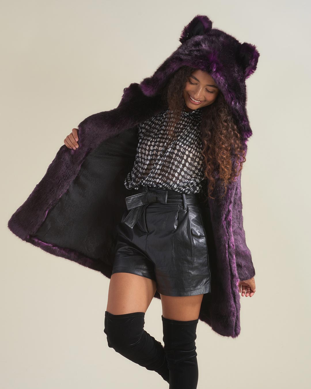 Looking down and smiling and leaning to one side with need bent, wearing purple midnight wolf faux fur jacket with hood and ears up. 