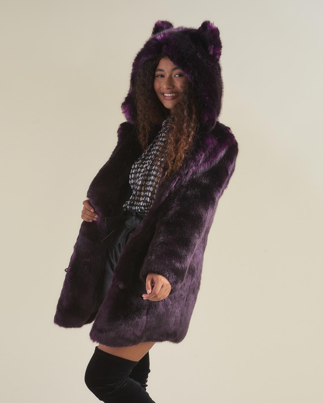 Female model facing slightly facing one side, smiling and holding open midnight wolf fake fur dark purple coat while wearing hood with ears up. 