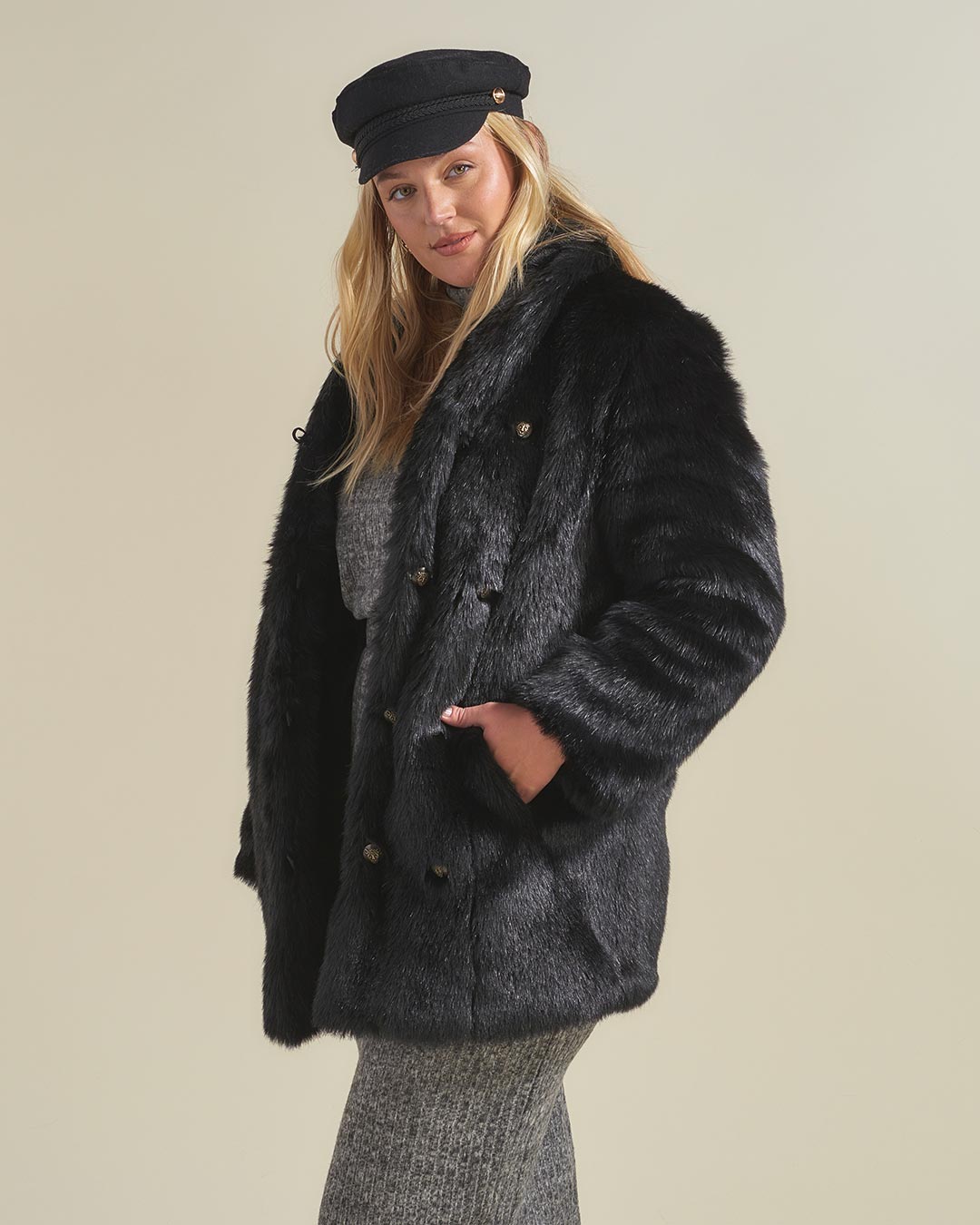 Blonde haired gal wearing paperboy hat standing slightly to one side with her hand in the pocket of a realistic black panther fur coat. 