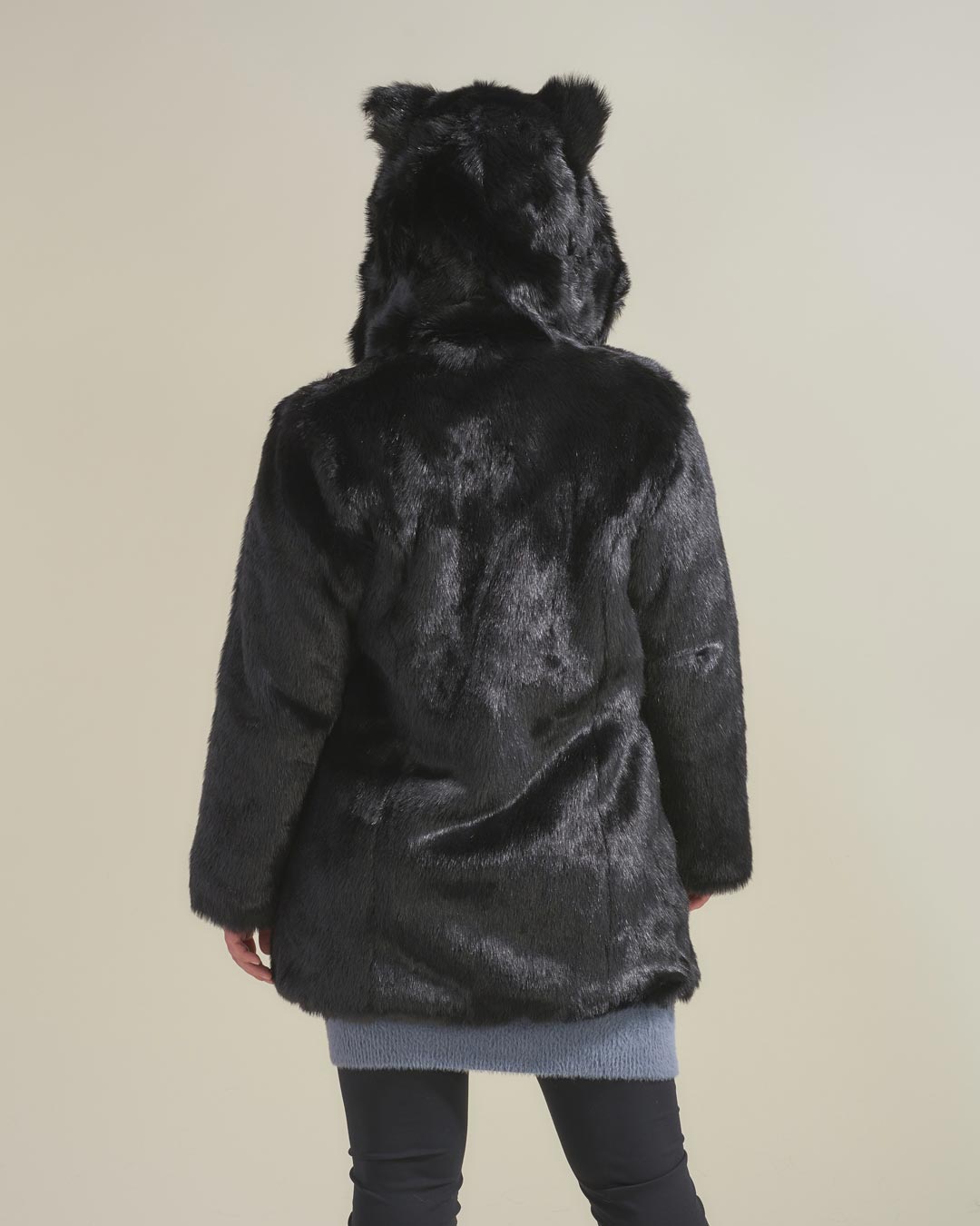 Women with back facing the camera, arms at her side, wearing fake fur black panther jacket with ears and hood on.