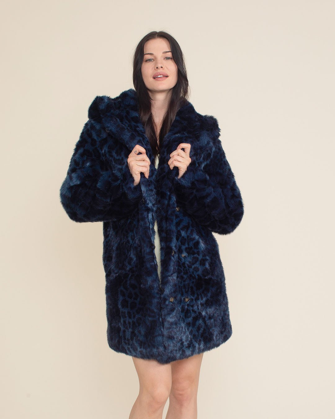 Flirty girl in the Indigo Leopard Classic Collector Edition Vegan Fur Coat, holding the upper lapels with the hood and ears down.