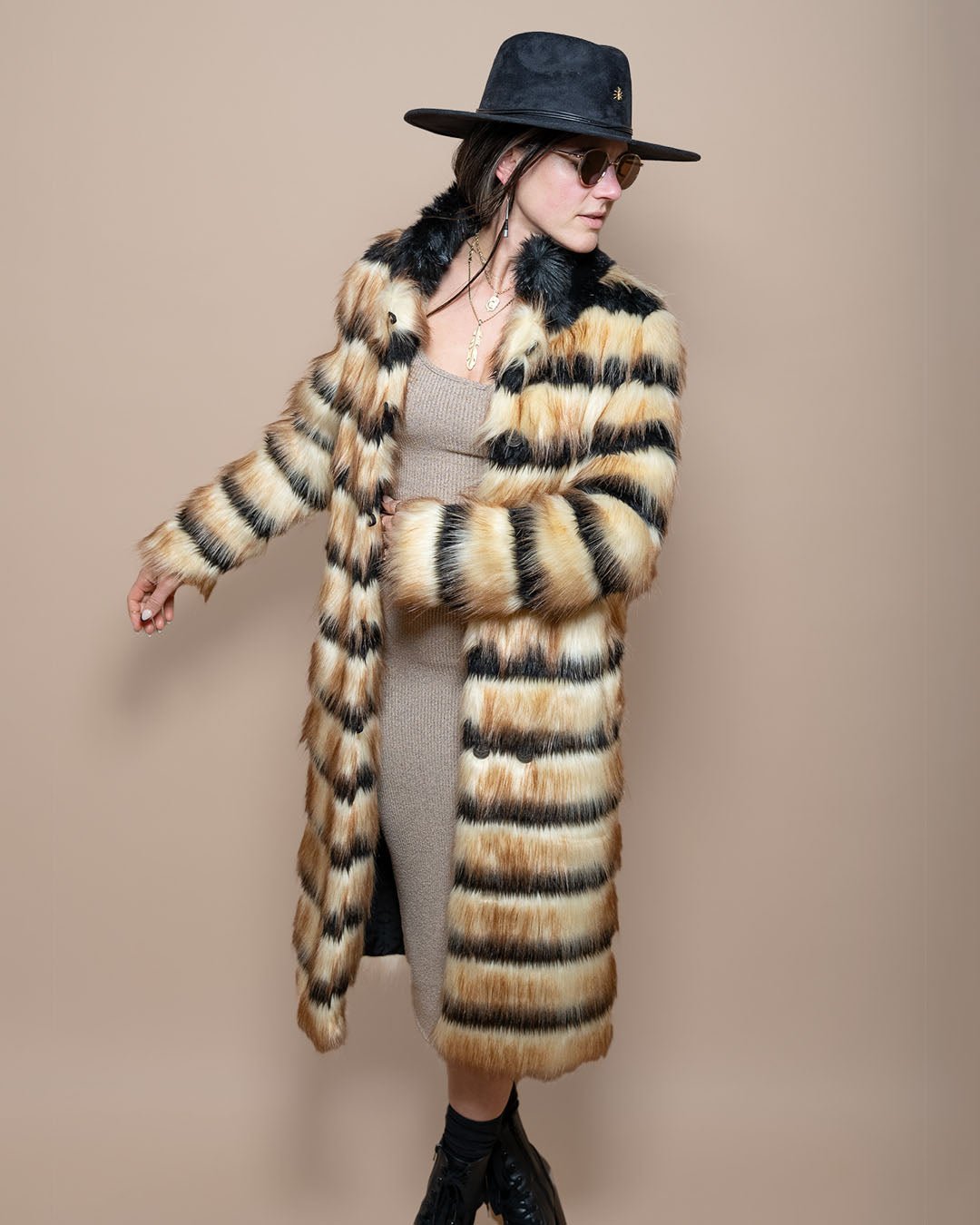 Girl in black fedora wearing Collared Gazelle Long Faux Fur Jacket, twisting with one arm out and the other bent, looking to the side.