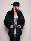 Man with beard and mustache wearing fedora wit his head turned to one side, while wearing black panther fake fur coat holding bottom sides with both hands. 