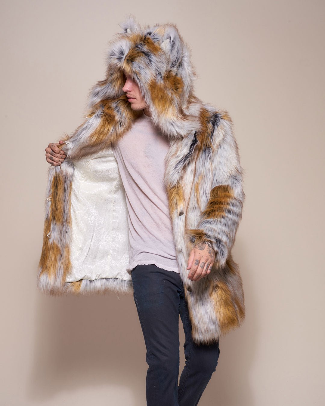 A male model in a faux fur Arctic Fox Classic Coat, tuned to one side and holding open one side of the coat to show off the inner liner, with the hood and ears up.