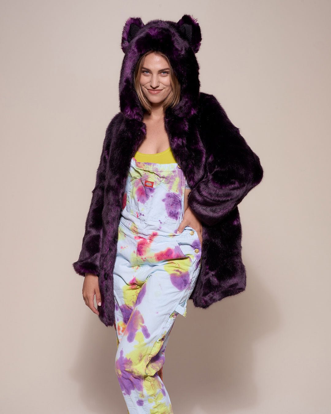 Smiling light brown haired girl with one hand on her waist wearing dark purple midnight wolf fake fur coat with hood and ears up. 