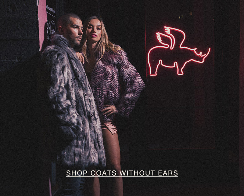 Man a women standing against a wall outdoors at night wearing faux fur coats and a button that says SHOP COATS WITHOUT EARS