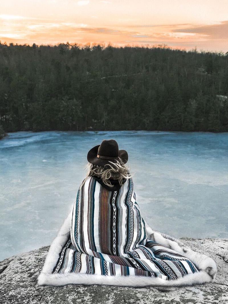 Female Wrapped in Husky Baja faux Fur Throw Sitting Beside a Lake