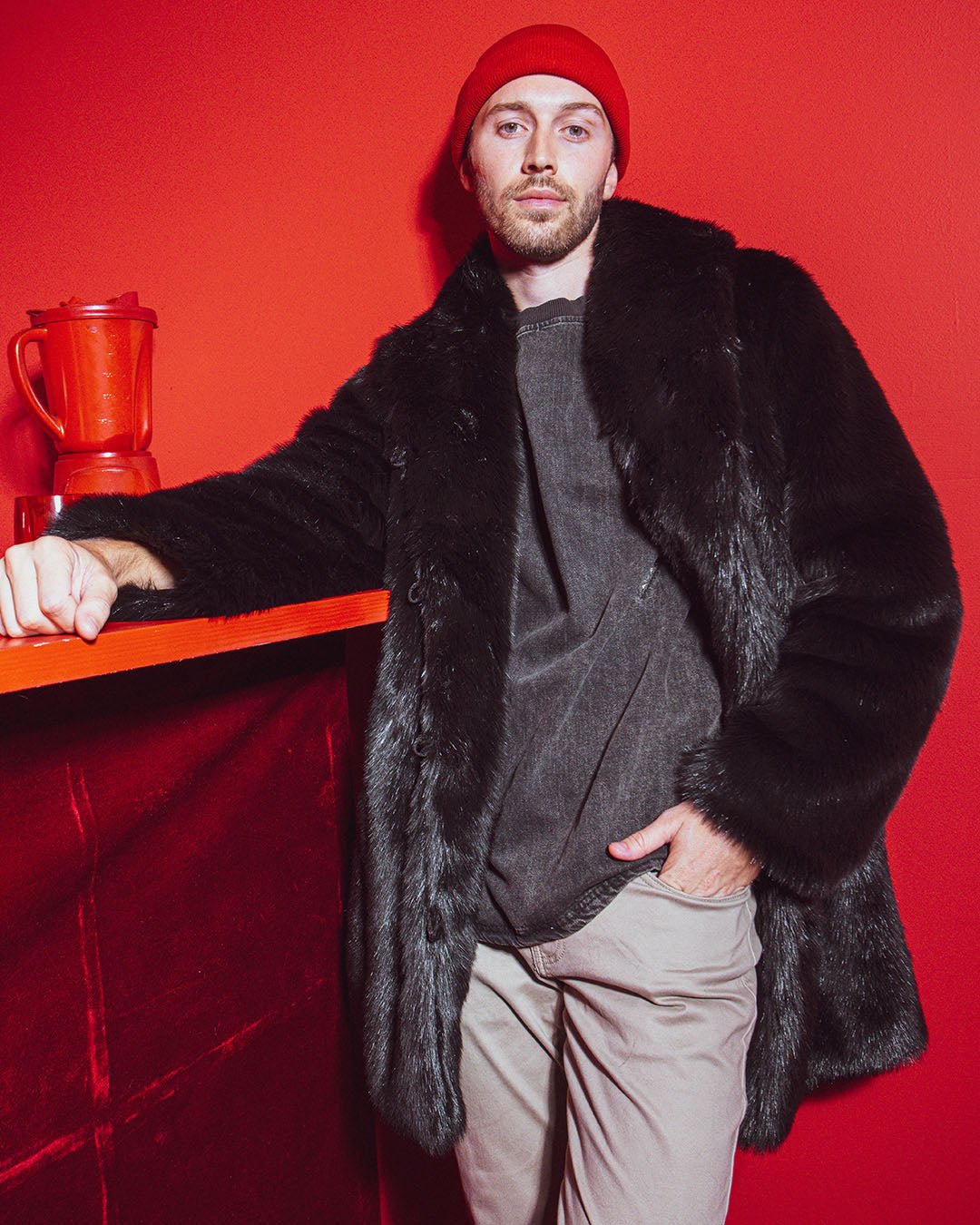 Dude in red beanie standing in a red room wearing collard black panther fake fur jacket. 