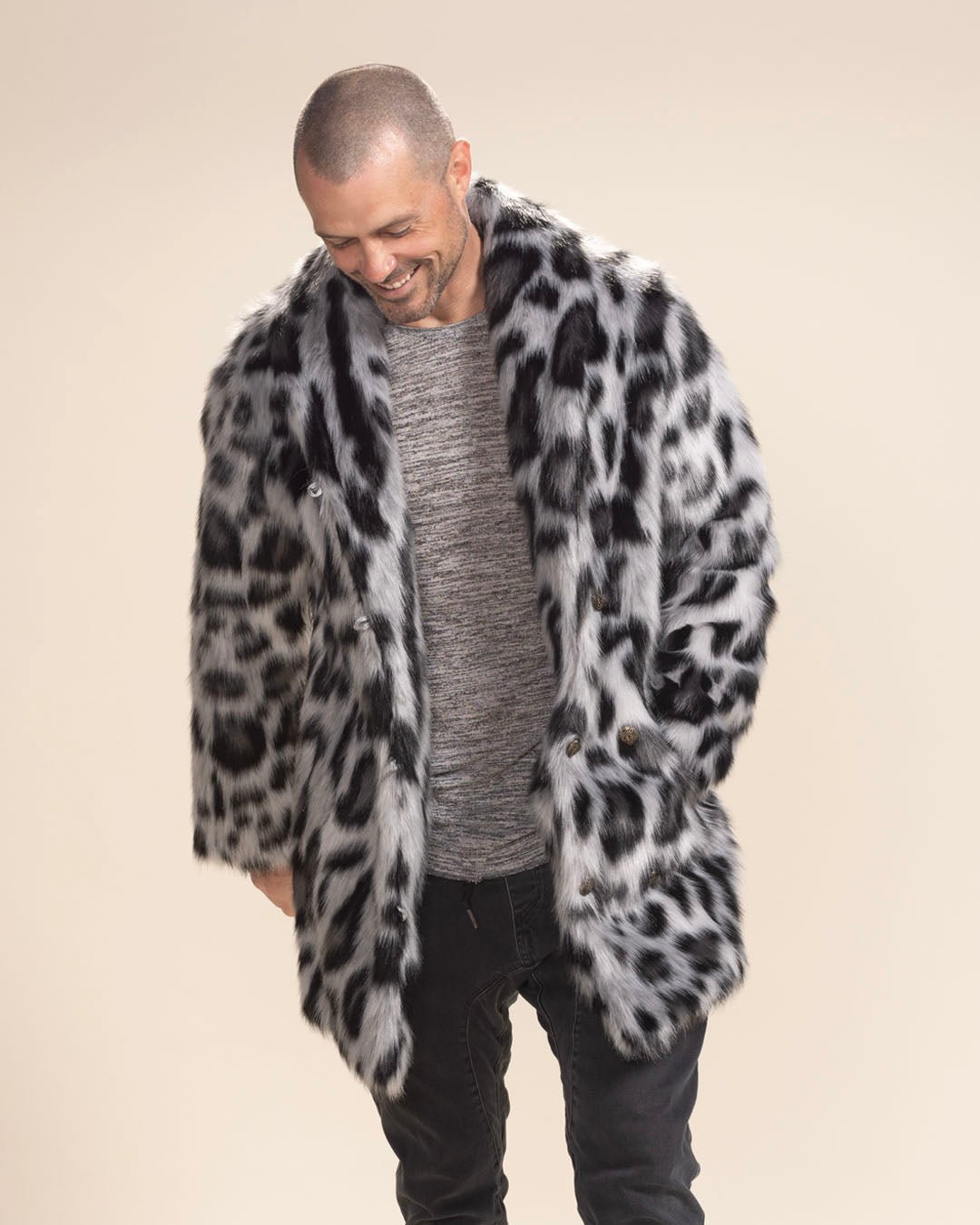 Handsome man smiles, looking down with hand in pocket of Collared Himalayan Snow Leopard vegan fur coat.