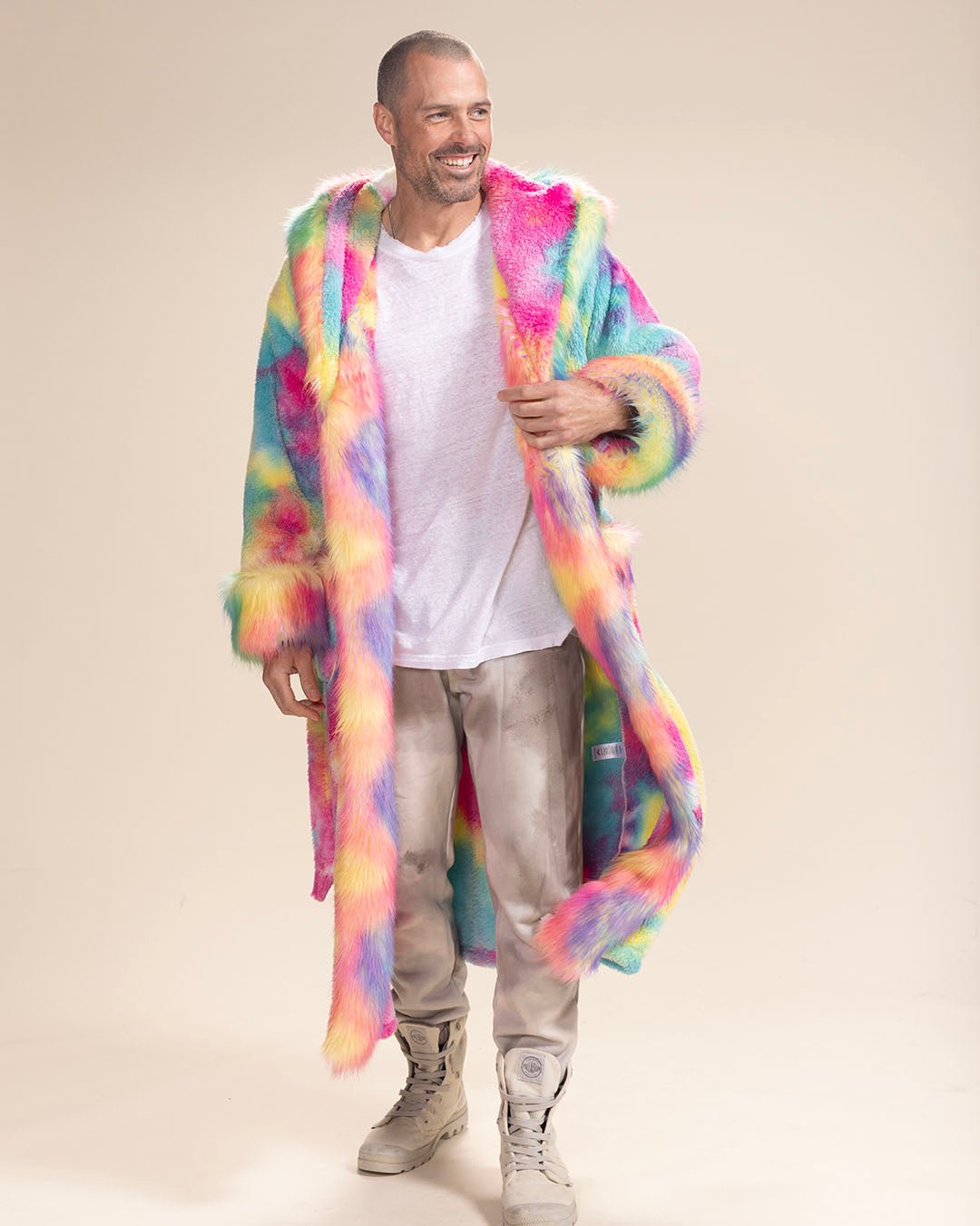 Smiling handsome man in Rainbow Bear vegan fur robe, holding one lapel with hood down—cozy and playful look.