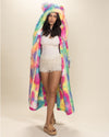 Kind-eyed dark-haired girl in open Rainbow Bear Vegan Fur Robe, hood and ears up, hands behind her back. Cozy and playful look.