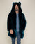 Kind-eyed man wearing the Classic Royal Wolf faux fur coat with the hood and ears on, one hand in his pocket, and the other out.