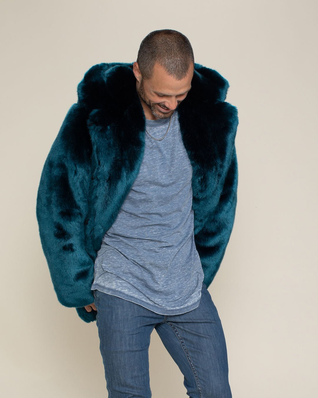 Handsome model with a crew cut smiles while looking down, wearing a Royal Wolf Classic vegan fur coat with the hood and ears down. 