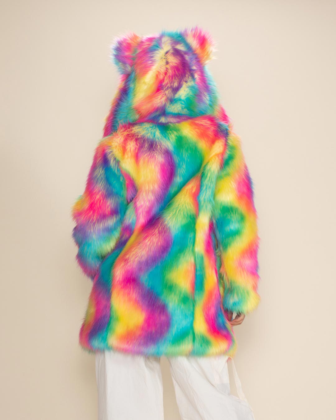 Sultry woman in Rainbow Bear Classic vegan fur jacket with hood and ears up, hands in pockets, posed against a white background.