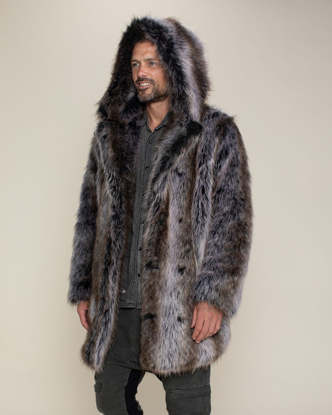 Male model with short mustache and beard facing slightly to one side with arms to his sides while wearing vegan fur grey wolf hooded coat.