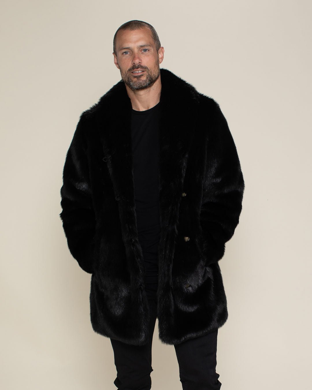 Handsome male model with very short beard and mustache facing the camera  with his hands in the pockets of a realistic fur black panther coat.