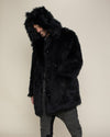 Male Model with a sly smile,  looking down standing slightly to the side with one hand in the pocket of fake fur black wolf coat with hood and ears.