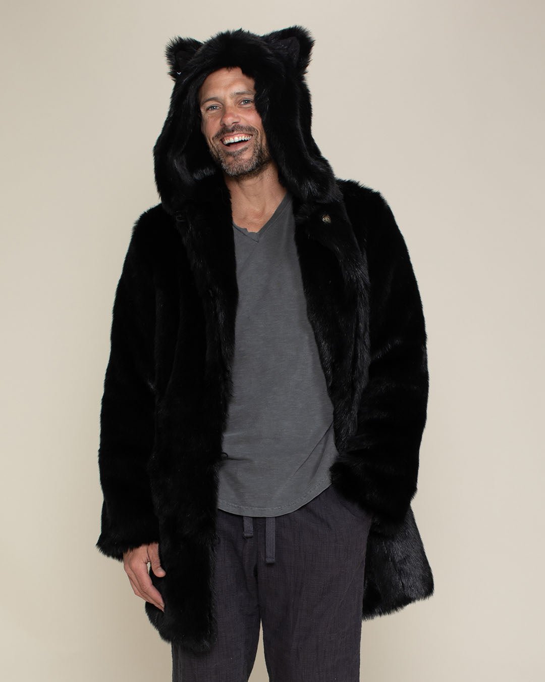 Laughing man with short beard and mustache with his hand in pants pocket wearing fake fur black panther coat with hood and ears. 