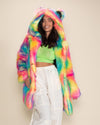 Joyful dark-haired model with one hand on the pocket of the Rainbow Bear Classic Fake Fur Jacket she's wearing, smiling confidently.