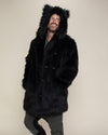 Smiling dude standing a bit sideways looking over to the side with his hands in the pockets of a realistic black wolf fur jacket. 