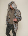 Slight side view of a male model wearing the Hooded Wolverine vegan fur coat, hood up, head down, and one hand in his pocket.