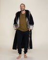 Smiling big, a handsome model with very short hair, a beard, and a mustache is wearing the open robe called the Grey Wolf, with faux fur on the sleeves and lapels.