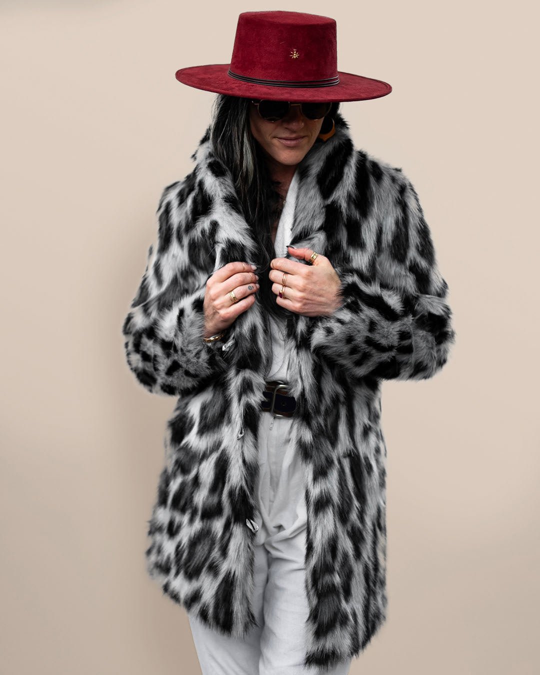 Chic woman in red fedora holding lapels of Collared Himalayan Snow Leopard Vegan Fur Coat. Fashion-forward, cozy faux fur style.