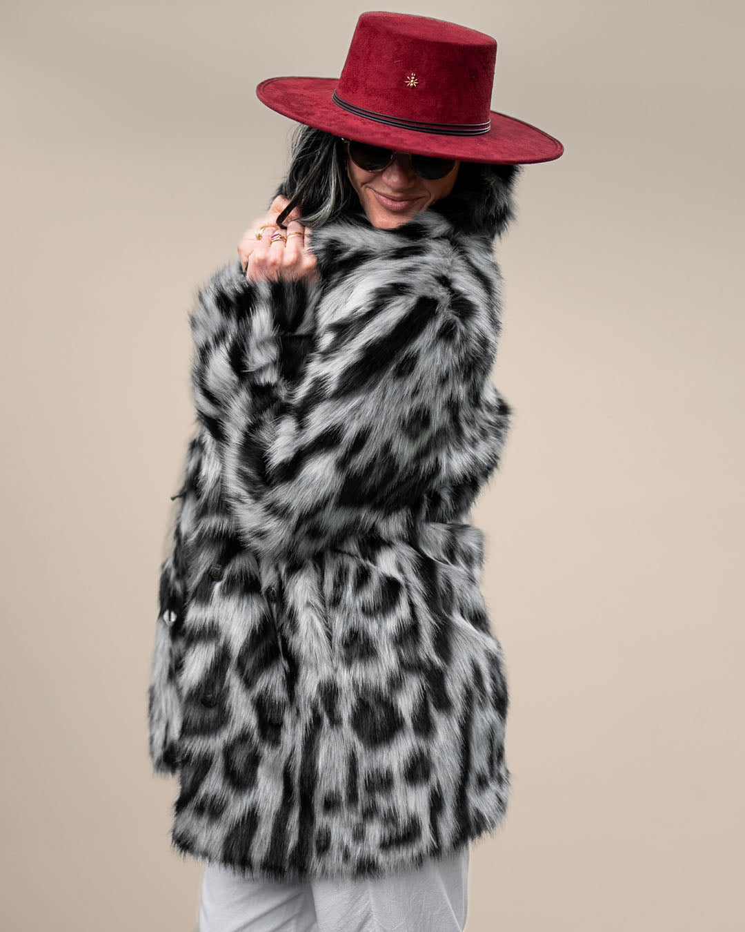 Dark-haired girl slightly smiling in red fedora and sunglasses, showcasing the side of the closed Himalayan Snow Leopard Collared faux fur jacket.