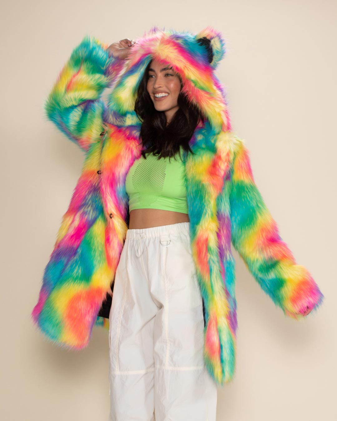 Smiling woman in Rainbow Bear vegan fur jacket, saluting with arm outstretched, slightly turned to one side for a playful pose. 