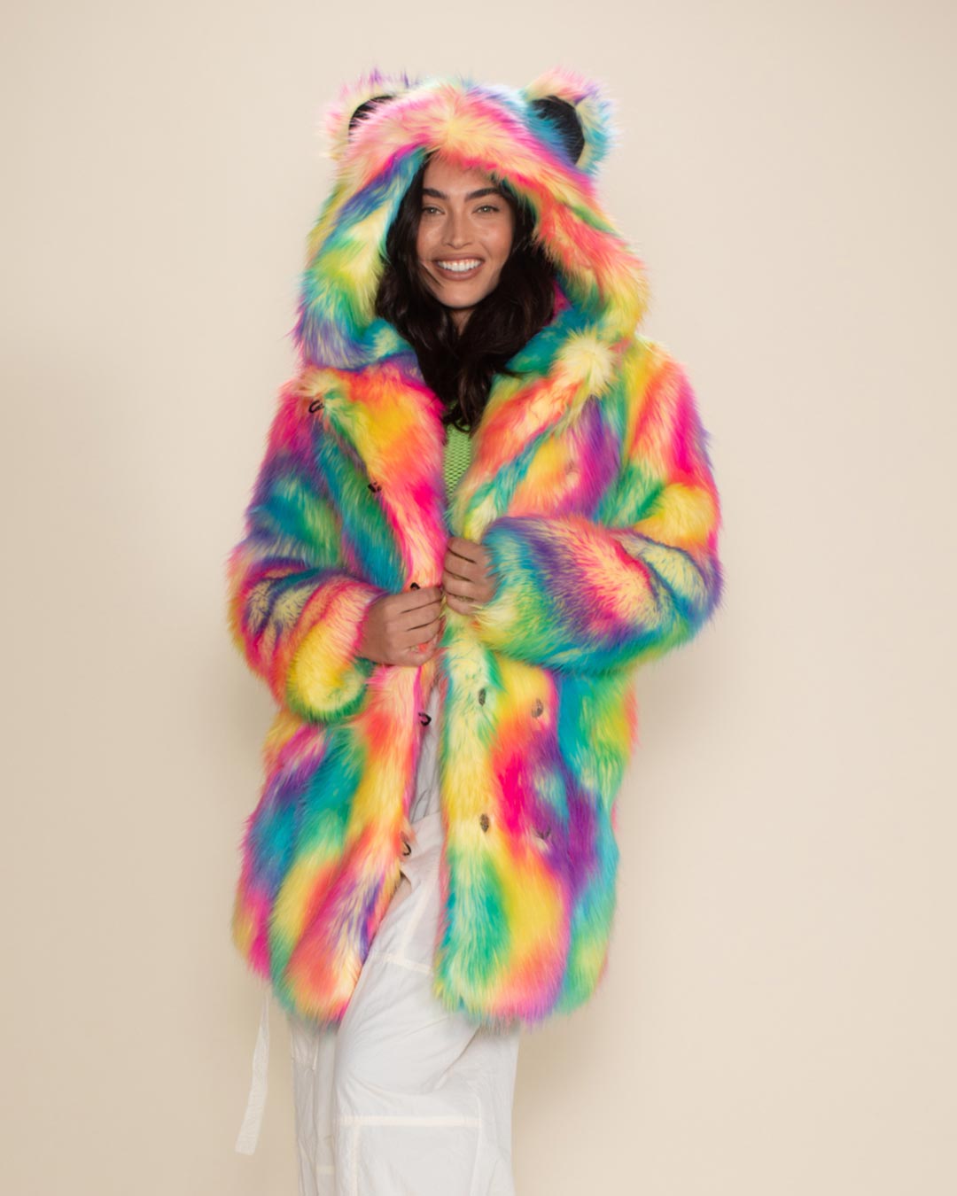 Happy dark-haired beauty in Classic Rainbow Bear Faux Fur Coat with hood and ears up, holding coat closed just under the lapels.