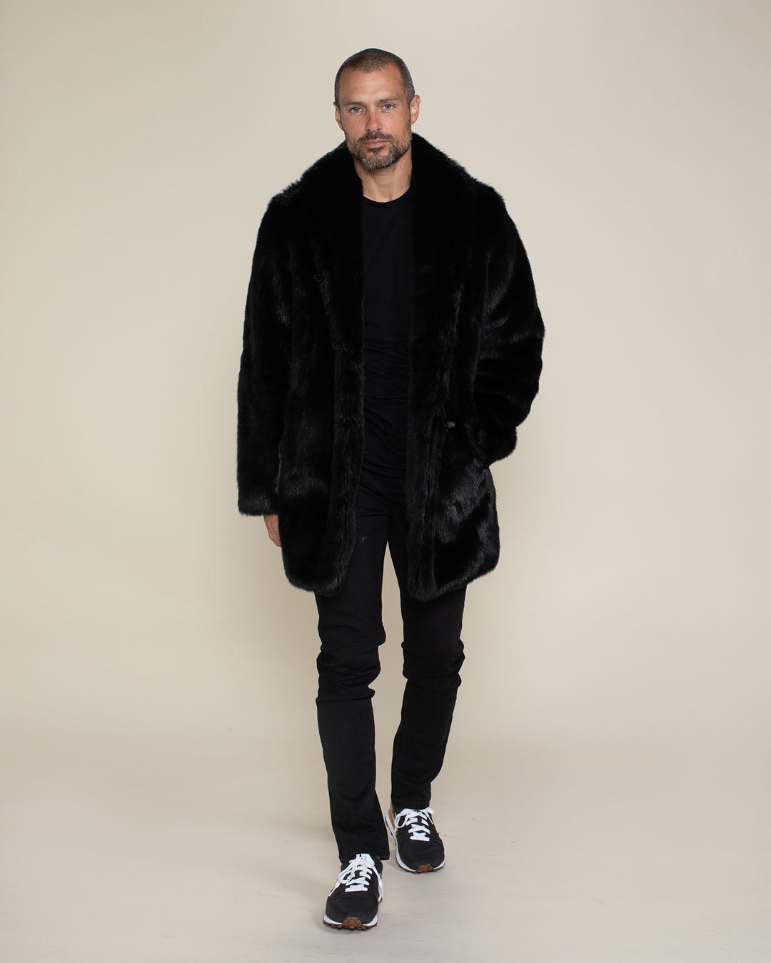 Handsome male model facing camera wearing fake fur black panther coat with one hand in his pocket. 