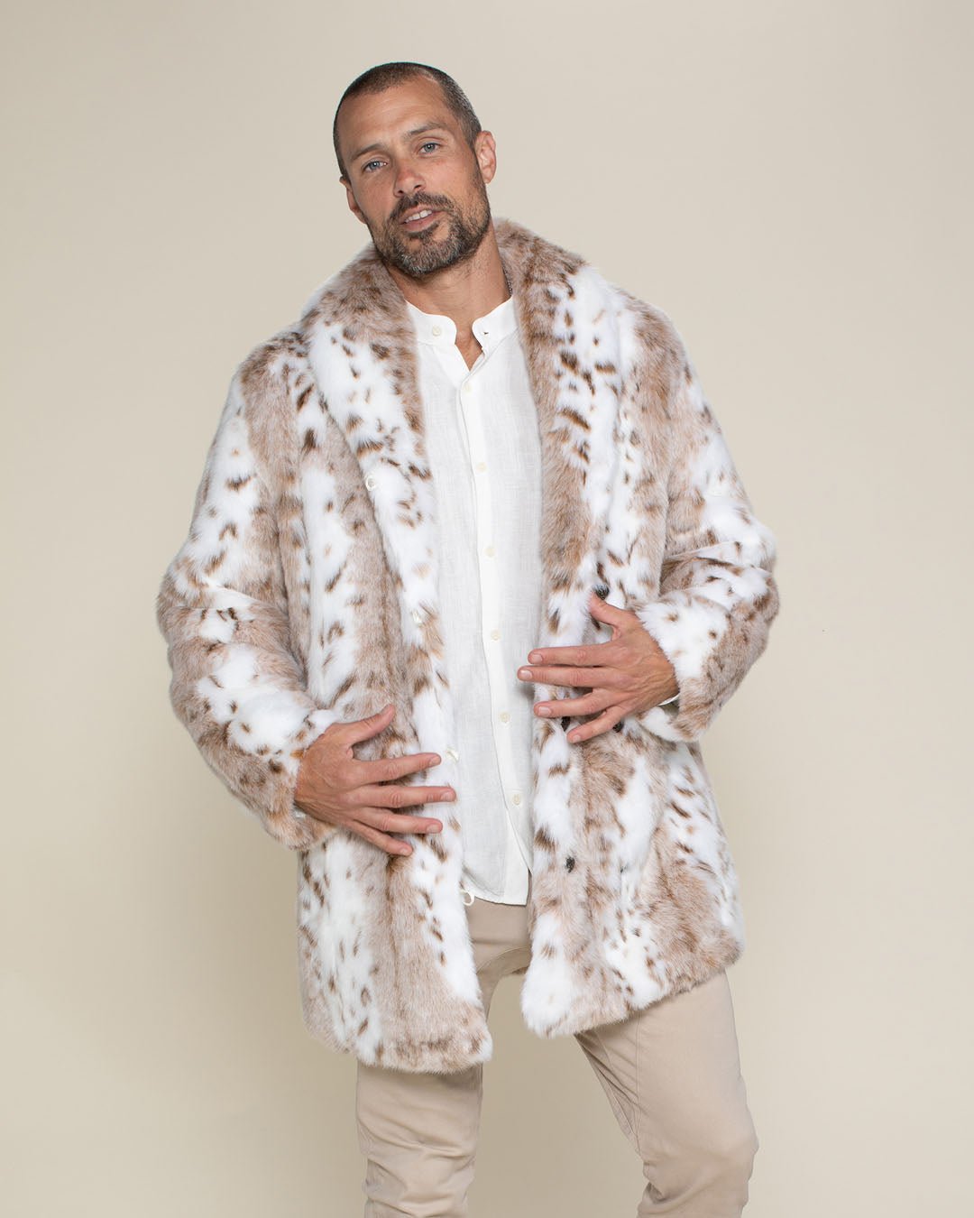 A handsomely bald male model with a flirtatious look on his face, slightly leaning to one side, has his hands resting on the outside bottom lapels of his open vegan Siberian snow leopard coat.