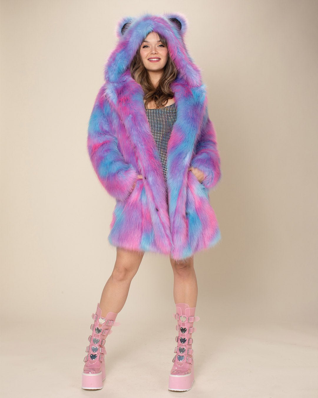 A smiling gal with her hands in the pockets of the Cotton Candy Bear fake fur jacket, hood and ears up, wearing pink platform buckle boots.