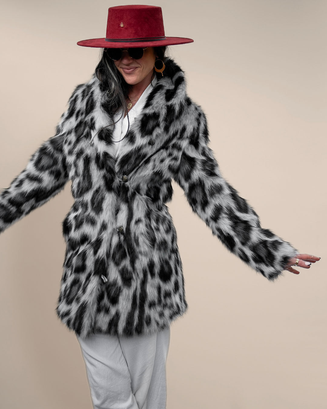 Smiling woman in red fedora with arms slightly outstretched, wearing button-up Collared Himalayan Snow Leopard Vegan Fur Coat. Chic look.