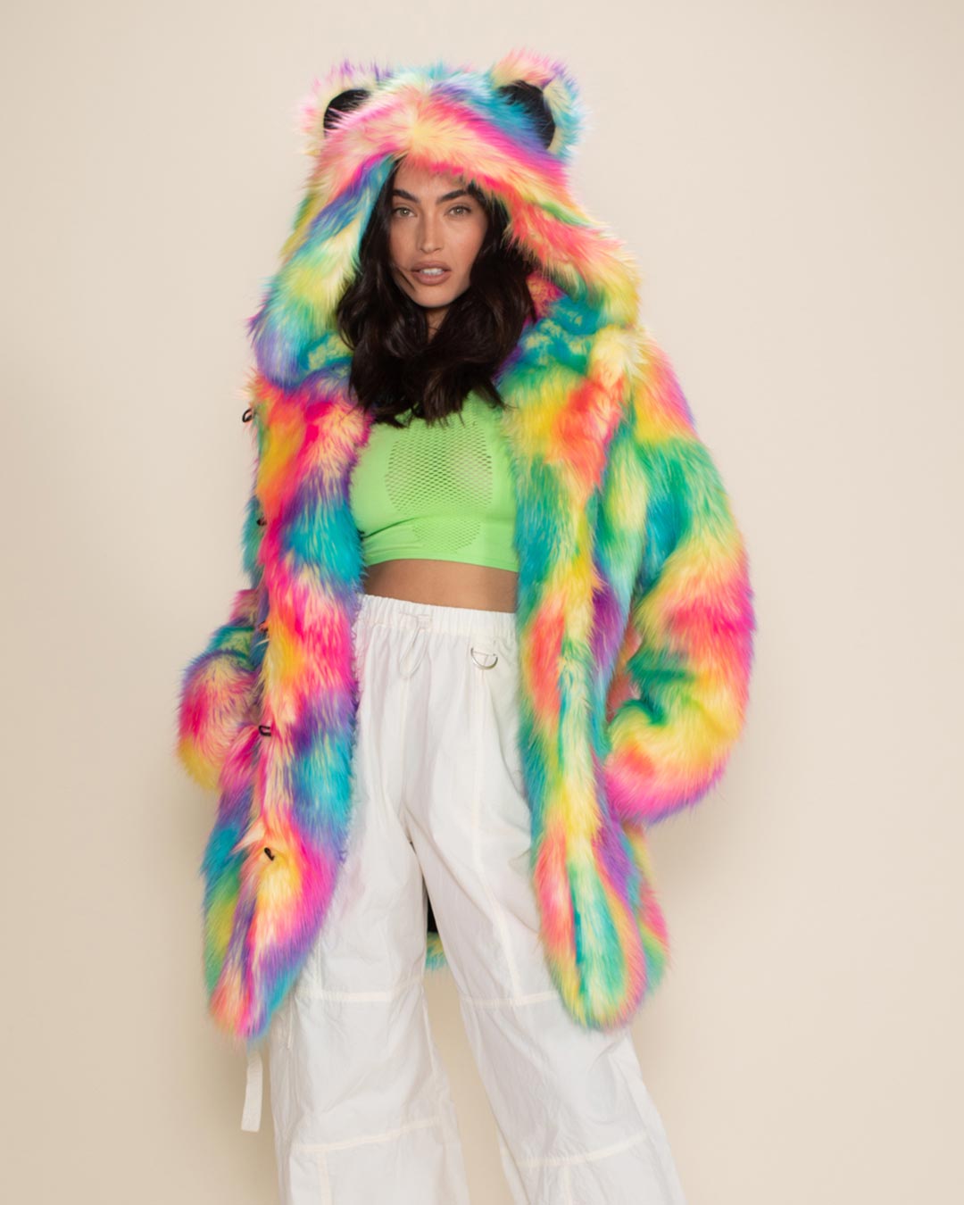 Sultry woman in Rainbow Bear Classic vegan fur jacket with hood and ears up, hands in pockets, posed against a white background.