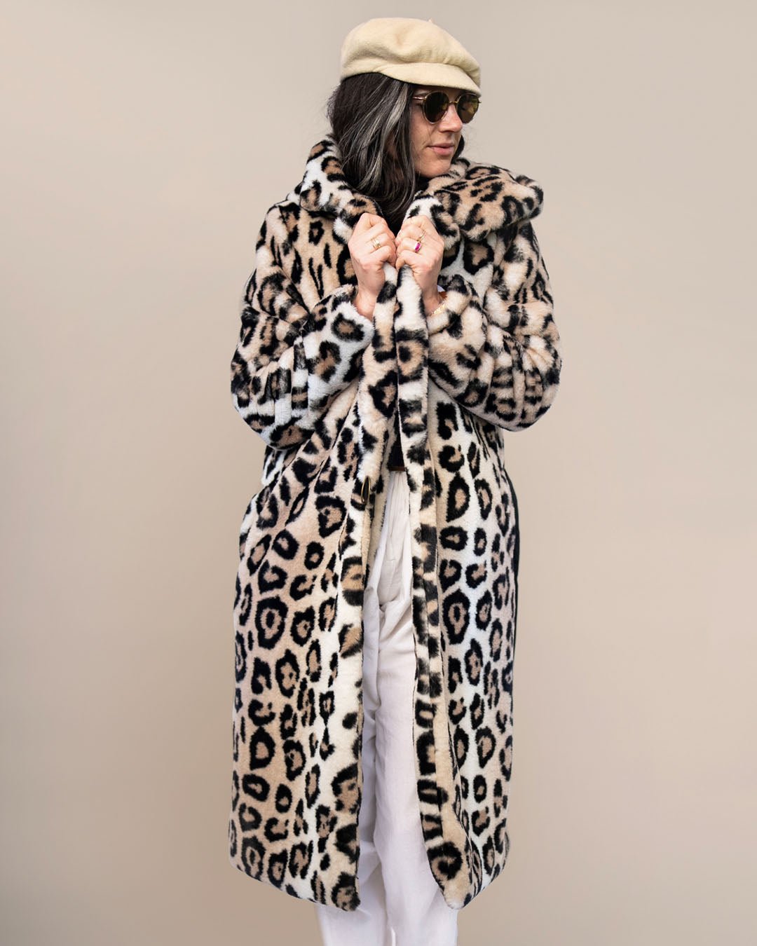 Dark-haired model in sunglasses, head turned to the side, in beige beret holding lapels of Classic Women&#39;s Long Faux Fur Coat in Arabian Leopard Print.