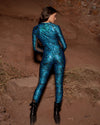 Woman standing facing red rock formations, showing the reflective snakeskin bodysuit from behind