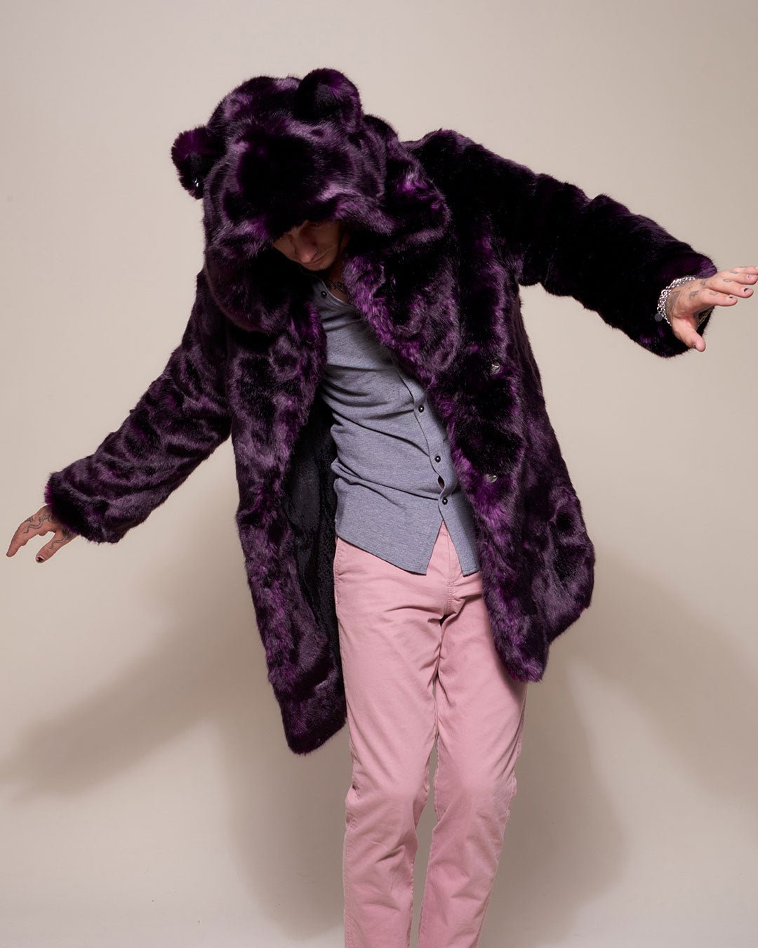 Male model looking down with arms out like an airplane,  wearing dark purple midnight wolf fake fur jacket with hood and ears. 