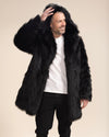 A male model is smiling while looking to one side, with one hand on the top of the hood of his fake fur black wolf jacket and the other hand at his side.