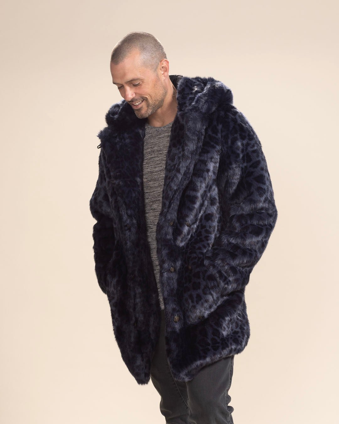 Very attractive nearly bald man smiling to himself, looking down with hands in the pockets of his Classic Indigo Leopard Collector Edition Faux Fur Coat.