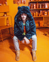 Male slightly smiling at the camera in an orange room, sitting and leaning forward in the Classic Indigo Leopard Collector Edition Faux Fur Jacket