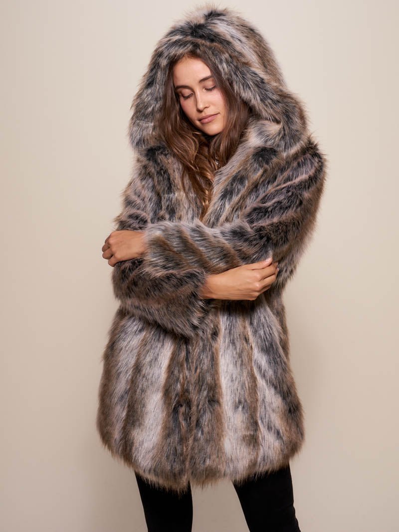 Smiling dark haired female model leaning against a painting while wearing hooded grey wolf fake fur coat.