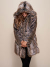 Smiling gal with fake fur grey wolf hooded coat over her eyes while her arms are crossed at her waist showing off entire coat. 